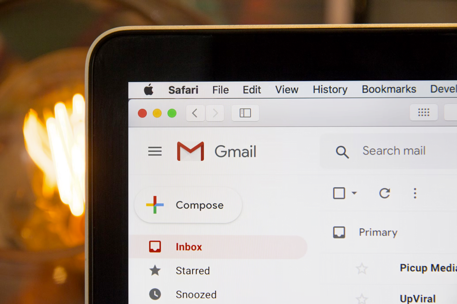 Gmail inbox opened in Safari browser on a computer screen, with 'Compose' and other email folders visible, and soft glowing lights in the background.